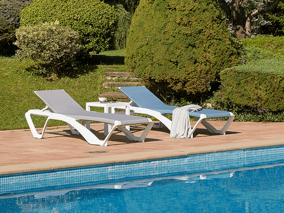 Modern sling chaise lounges beside a swimming pool, featuring breathable fabric seating designed for comfort and quick drying.